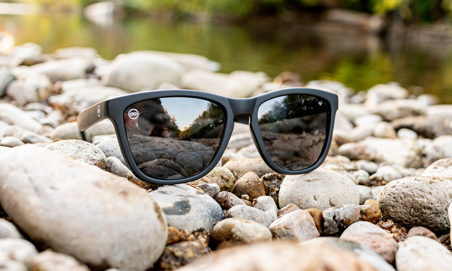 black sunglasses sitting on smooth river rocks
