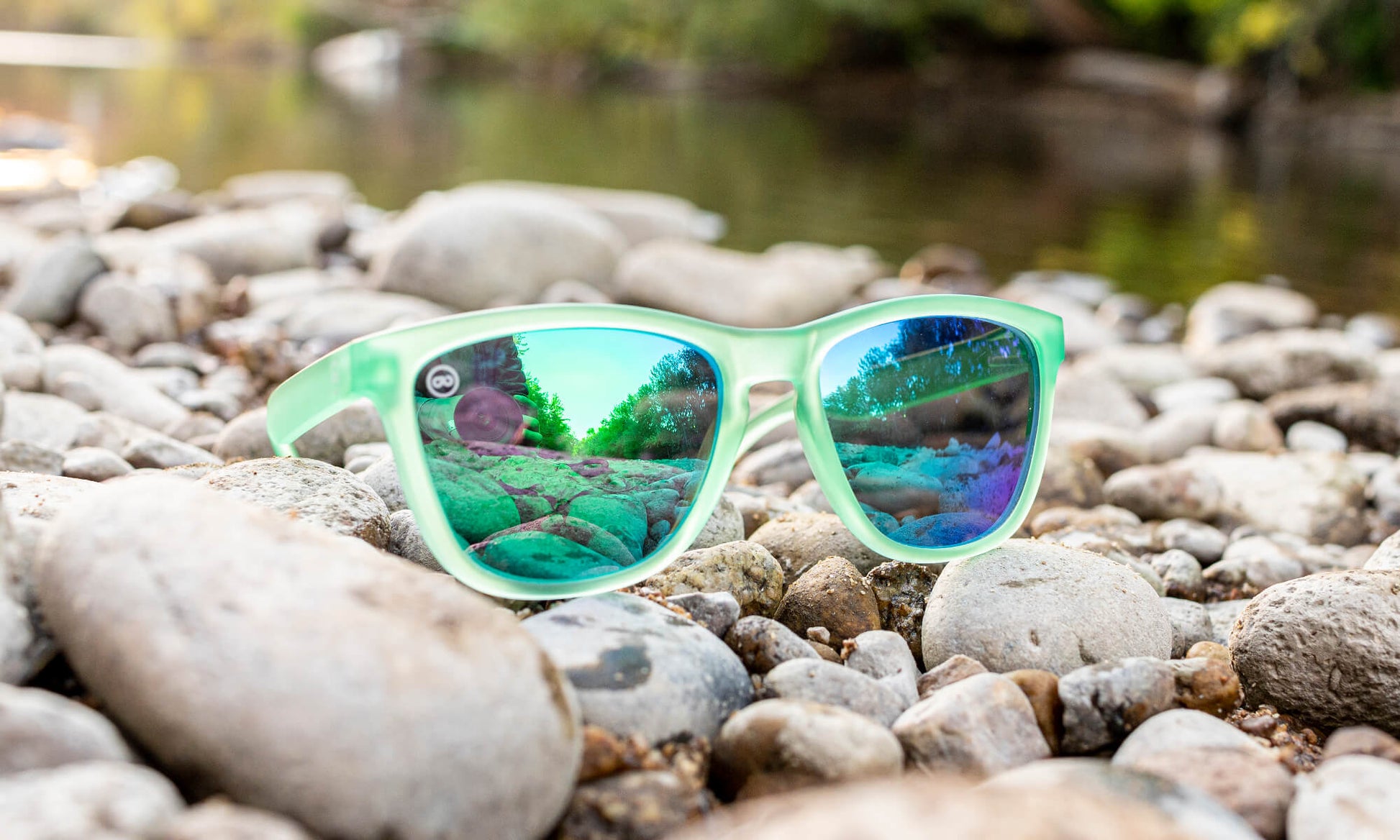 green sunglasses sitting by a river on smooth river rocks